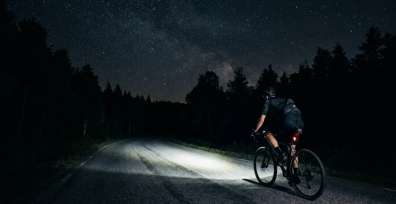 Cycliste roulant sur route de campagne non éclairée la nuit avec un puissant phare avant illuminant l'asphalte