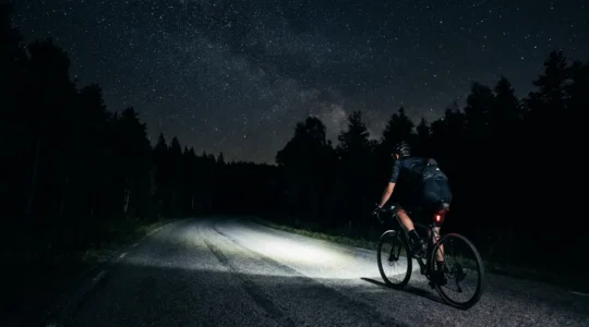 Cycliste roulant sur route de campagne non éclairée la nuit avec un puissant phare avant illuminant l'asphalte